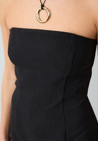 Abito nero senza spalline con righe verticali, design aderente, tessuto testurizzato e collana con pendente ad anello dorato per un tocco in più.