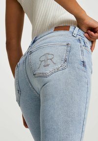 Jeans de mezclilla azul claro con un diseño ajustado, bolsillos traseros con el logo bordado "RR" y una etiqueta de cuero en la cinturilla.