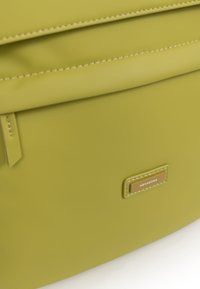 Groene vegan leren rugzak met een gladde textuur, bovenflap sluiting, gouden merkplaat en contrasterende stiksels.