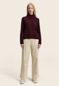 Maglione a collo alto di colore bordeaux con texture a coste, abbinato a pantaloni a gamba larga di un beige chiaro e scarpe con plateau di colore crema.