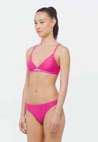 Růžový bikini set s trojúhelníkovým topem s tenkými ramínky a odpovídajícími krajkovými kalhotkami, vyrobený z hladké tkaniny s logem na topu.