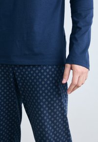 Camisa de manga larga en color navy combinada con pantalones de pijama estampados que presentan un diseño de diamantes en azul claro. Material de algodón suave, corte relajado.