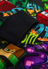 Colorful, graphic patterned fabric with a black ribbed cuff; includes designs of characters and shapes in bright hues against a dark background.