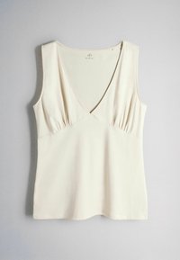 Haut sans manches couleur crème avec un col en V profond et de subtiles fronces sous la poitrine, posé à plat sur un fond gris.