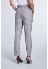 Pantalons gris à carreaux avec une coupe décontractée, chevilles effilées et poches arrière, accompagnés de chaussures à talons hauts noires avec un motif serpent.