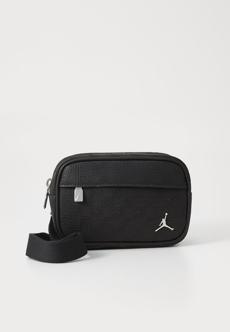 Schwarze rechteckige Tasche aus strukturiertem Material. Verfügt über einen silbernen Reißverschluss, einen Tragegurt und ein auffälliges Jordan-Logo auf der Vorderseite. Gemusterte Oberfläche.
