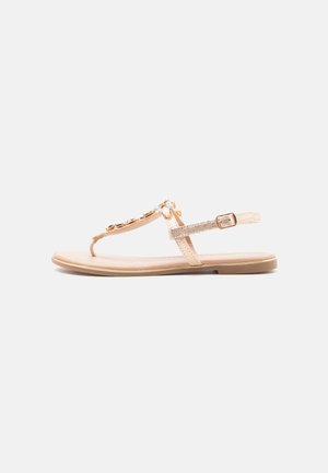 Beige flad sandal med tynde remme, spænde lukning og dekorative ædelstene langs den øverste rem.