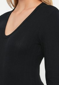 Sort ribbet langærmet top med en dyb V-hals og slim fit, der har subtil tekstur og en ren finish.