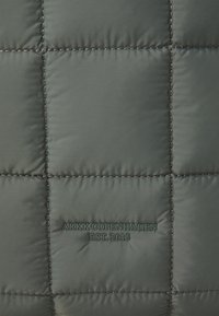 Tissu matelassé vert avec une texture lisse. Présente un texte en relief "ARKK COPENHAGUE EST. 2015" en vert foncé en bas.