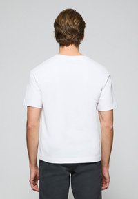 Biała bawełniana koszulka z okrągłym dekoltem i krótkimi rękawami. Charakteryzuje się prostym krojem i minimalistycznym designem, bez wyraźnych wzorów czy akcentów.