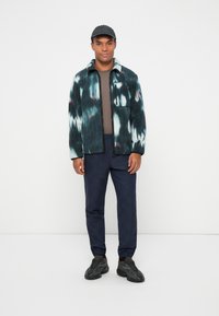 Fleece jacket with green and white tie-dye pattern, gray crew neck shirt, navy checkered pants, and dark sneakers.