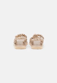 Beige slip-on sandaalit, joissa on rypistetyt kangasvarret, pehmeät pohjat ja tasainen muotoilu, jotka tarjoavat sileän pinnan ja minimalistista tyyliä.