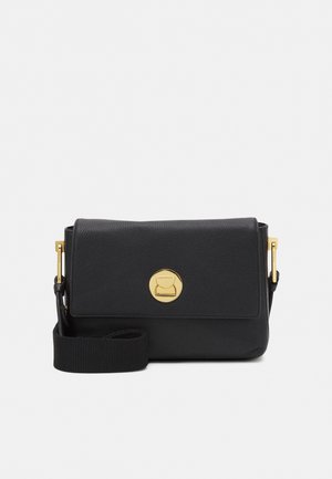 Sac bandoulière en cuir noir avec fermoir circulaire doré et sangle large en tissu réglable sur fond uni.