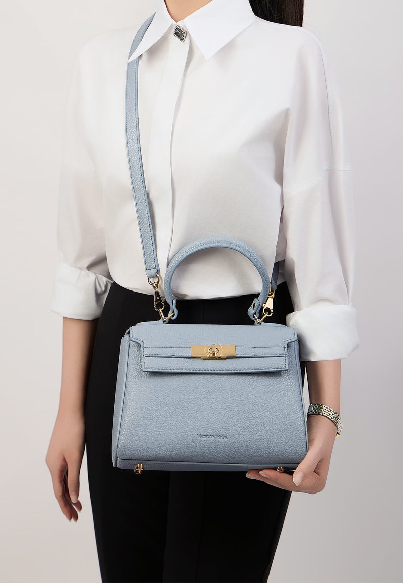 Borsa a mano in pelle azzurro chiaro con un design strutturato, manico superiore, tracolla rimovibile e chiusura in tono oro. Dettaglio della superficie texturizzata.