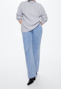 Maglione grigio chiaro a coste abbinato a jeans in denim blu a vita alta con gamba dritta e spacco frontale, completato da stivali neri.