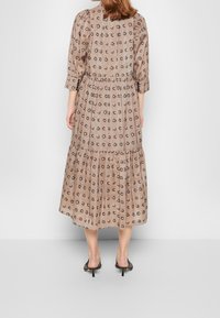 Bruna mekko, jossa on kukkakuosi, kolmivartiset hihat, kerroksellinen vyötärö ja kerrostettu hame. Valmistettu kevyestä kankaasta, jossa on virtaava rakenne.