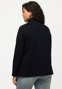 Giacca in pile blu navy con colletto alto, maniche lunghe e taglio dritto. Presenta una texture liscia e semplici dettagli di cucitura.