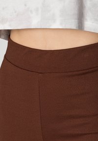 Les leggings marron présentent un tissu lisse et extensible avec une taille large. La coupe est ajustée, mettant en avant une texture sans couture.