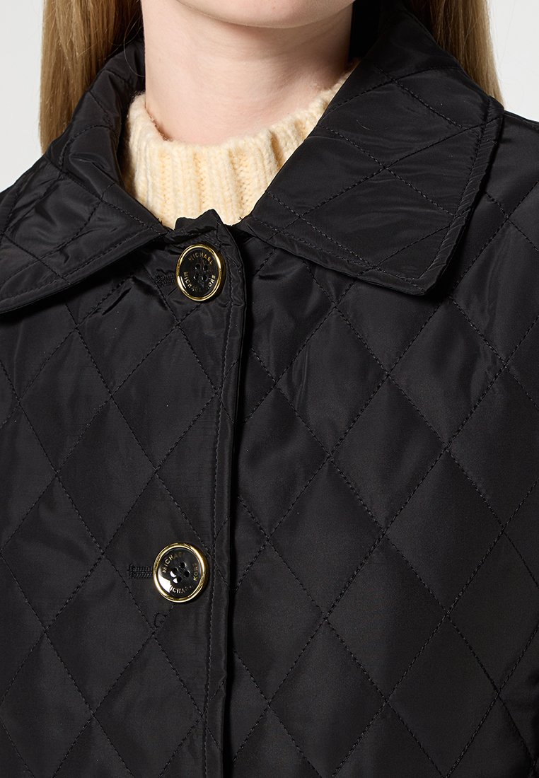 Veste matelassée noire avec un col classique, ornée de boutons dorés et d'une texture lisse et brillante. Le tissu présente un motif en losange.