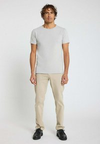 T-shirt ajusté gris clair en tissu doux, associé à un pantalon beige et des chaussures noires. Design simple, manches courtes et col rond.