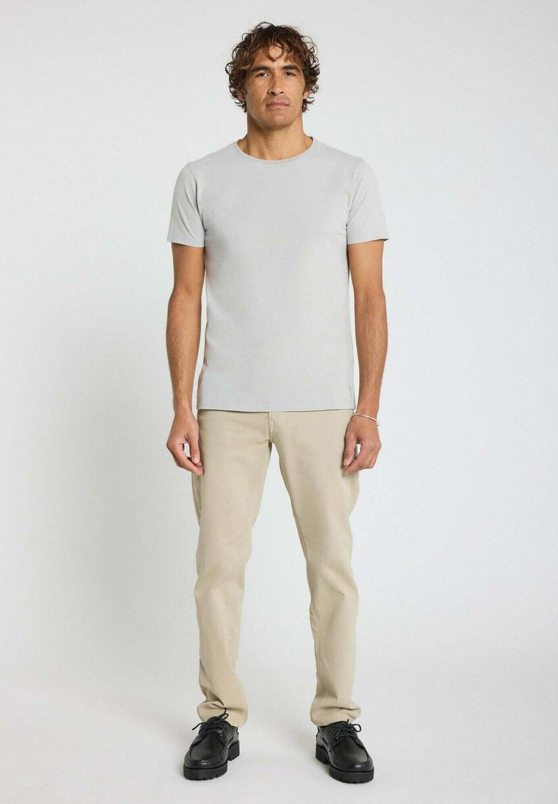 T-shirt ajusté gris clair en tissu doux, associé à un pantalon beige et des chaussures noires. Design simple, manches courtes et col rond.