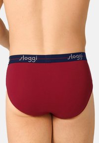 Bordeauxfarbene Baumwollslips mit einem marineblauen elastischen Bund, der den Markennamen "sloggi" in Hellgrau zeigt. Glatte Textur, klassischer Schnitt.