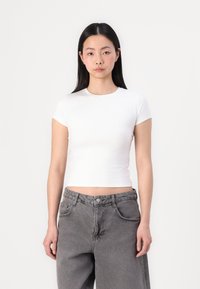 Hvit crop-top med korte ermer, rund hals, jevn tekstur. Kombinert med høyt liv, falmede grå vide jeans med lommer.
