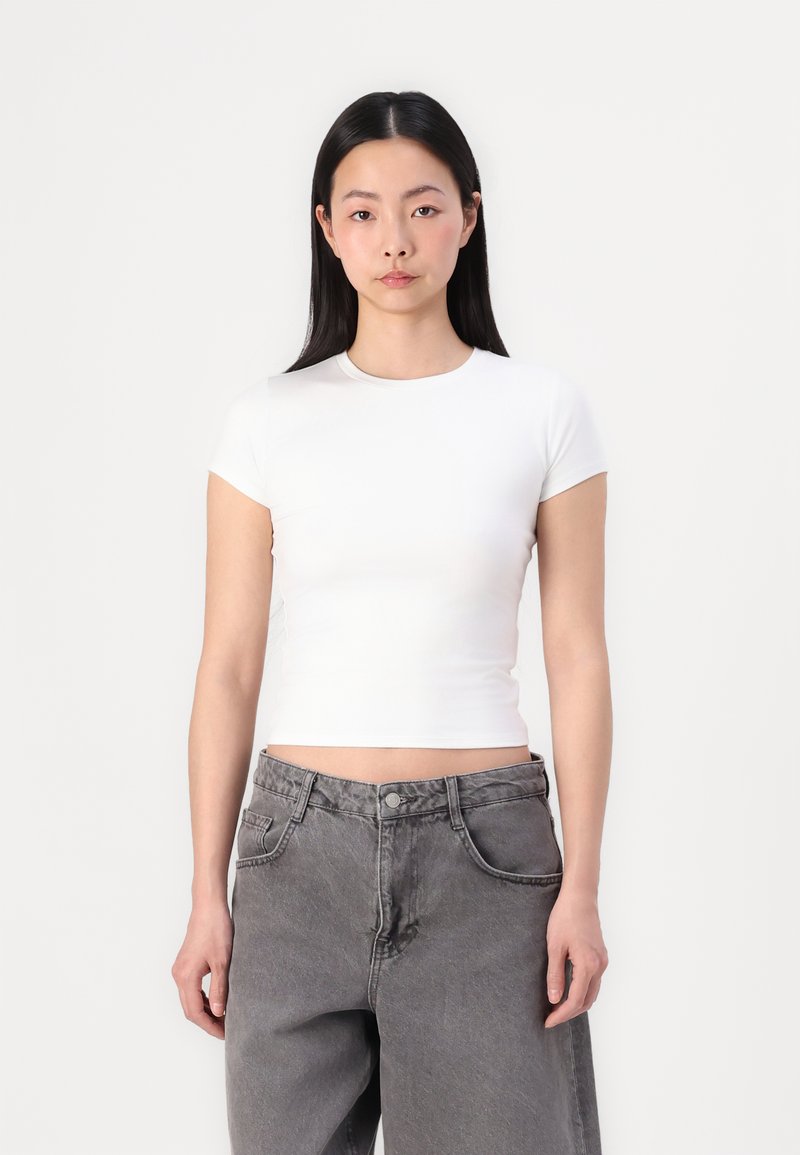 Hvit crop-top med korte ermer, rund hals, jevn tekstur. Kombinert med høyt liv, falmede grå vide jeans med lommer.