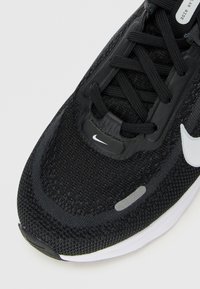 Sule lähedalt must Nike jooksusaabas, millel on võrkkangast ülemine osa, paelad, valge swoosh logo ja peegeldav riba varvaste piirkonnas.