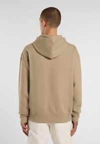 Felpa beige con cappuccio e vestibilità comoda, caratterizzata da una consistenza morbida e polsini a coste, presentata da dietro.