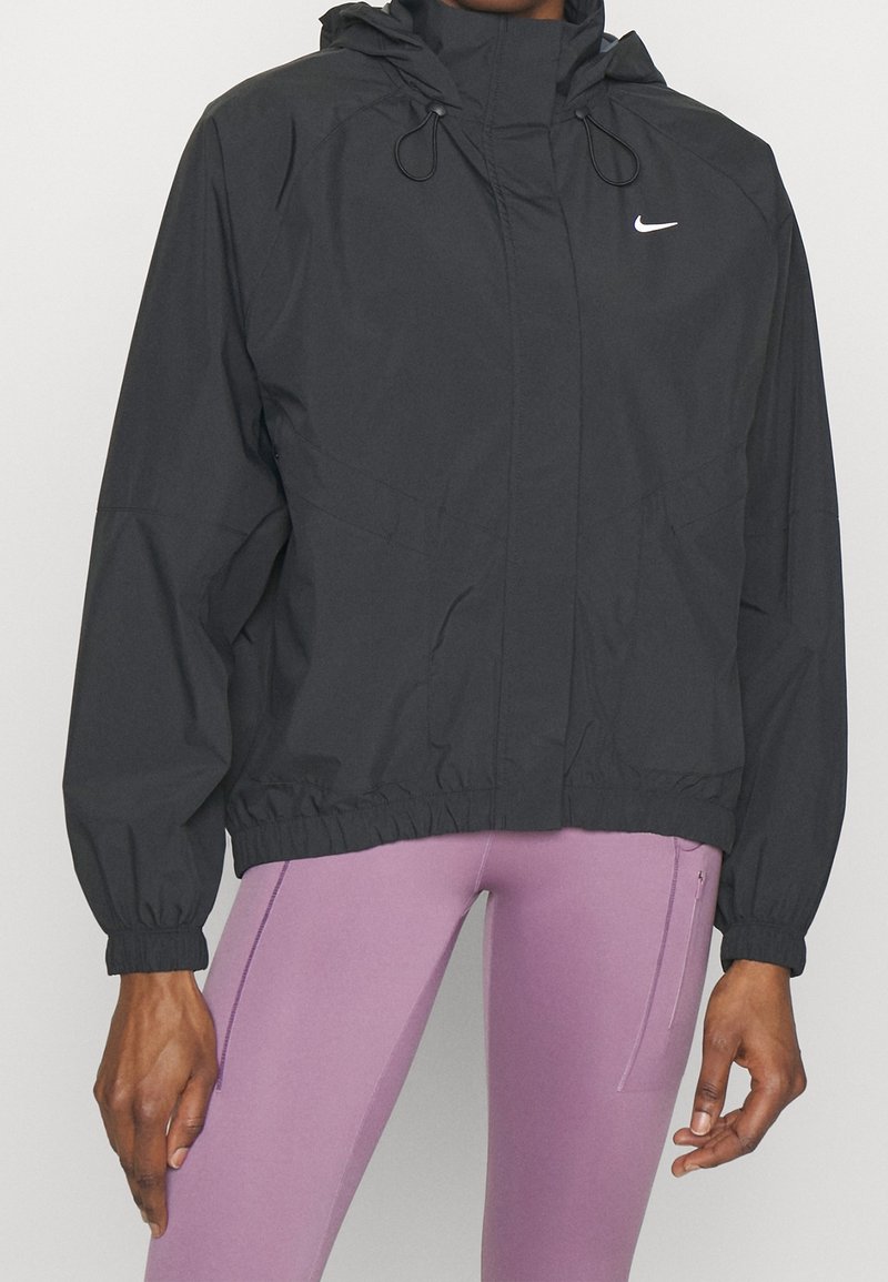 Černá větrovka s vysokým límcem, kapucí, elastickými manžetami a stahovacím pasem. Na hrudi má malé bílé logo.