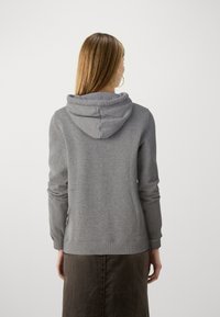Sudadera gris con un acabado texturizado, que presenta una capucha con cordón y puños acanalados. La prenda se lleva sobre una falda de color oscuro.