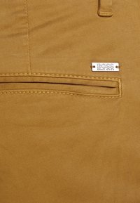 Beżowa bawełniana tkanina o teksturowanej powierzchni, z kieszenią na zamek błyskawiczny i metalową srebrną tabliczką z logo BOSS.