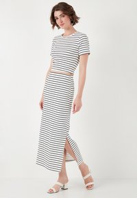 Completo a righe composto da un crop top aderente e una lunga gonna con spacco laterale, realizzato in un tessuto morbido e leggero nei colori bianco e nero.