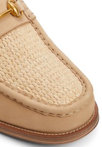 Zapato deslizante de color beige claro con una parte superior de tejido similar a la paja, ribete de cuero suave y suela de madera con costuras visibles. Acento de herrajes dorados.