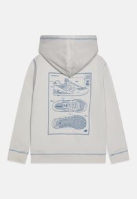 Jasnoszara bluza z kapturem z niebieską graficzną ilustracją butów New Balance na plecach, z prążkowanymi mankietami i dołem.