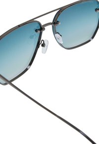 Gafas de sol con un marco de metal oscuro, forma hexagonal, lentes de degradado azul y almohadillas nasales transparentes. Las patillas delgadas se extienden desde el marco.