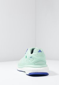 Jasnozielony but do biegania z siateczkową cholewką, niebieskimi akcentami i białą podeszwą środkową z technologią "boost". Wyściełany kołnierz dla komfortu.