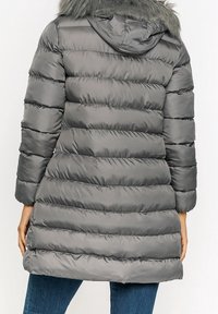 Šedý prošívaný péřový kabát s vodorovným prošíváním, kapucí lemovanou umělou kožešinou a středně dlouhým střihem. Má dlouhé rukávy a lesklý povrch.