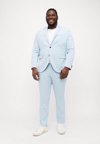 Helleblaue Anzug aus glattem Stoff, bestehend aus einem Ein-Knopf-Blazer, passender Hose und weißen Sneakers darunter.