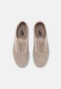 Une paire de baskets Vans en daim beige avec des lacets, des semelles en caoutchouc grises, et le logo Vans visible à l'intérieur de chaque chaussure, présentées de dessus sur un fond blanc.