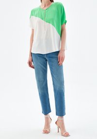 Haut à manches courtes avec un design bicolore vert et blanc, doté d'une fermeture éclair à l'avant. Associé à un jean bleu clair et des talons à brides.