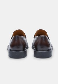 Mocassins en cuir marron avec une finition lisse, bout rond et une semelle en caoutchouc noir à faible épaisseur, présentant un doublure beige contrastante et des coutures détaillées.