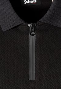 Sort tekstureret polo-shirt med en halv lynlås og sort ribstrikket krave, med et Schott N.Y.C.-mærke inde i halsudskæringen.