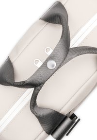 Beige színű táska fekete, texturált fogantyúkkal, fehér cipzárral és fémes részletekkel. Két grommettel és egy polírozott snap gomb részlettel rendelkezik.