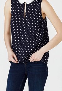 Blusa senza maniche blu navy con pois bianchi, caratterizzata da una scollatura a goccia frontale e un colletto Peter Pan bianco. Tessuto morbido, vestibilità comoda.