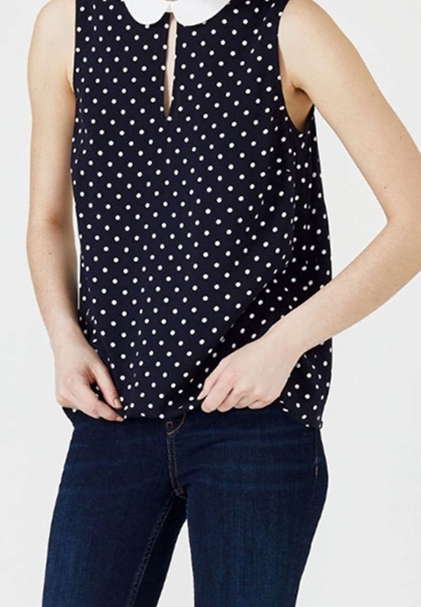 Blusa senza maniche blu navy con pois bianchi, caratterizzata da una scollatura a goccia frontale e un colletto Peter Pan bianco. Tessuto morbido, vestibilità comoda.