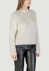 Witte, fluffy trui met een hoge halslijn, lange mouwen en een korte zoom, gecombineerd met zwarte leren broek. Zachte textuur en minimaal ontwerp.