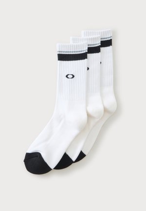 Trois paires de chaussettes blanches mi-mollet avec des bouts noirs, des rayures noires et grises en haut, et un petit logo ovale noir sur chaque chaussette.