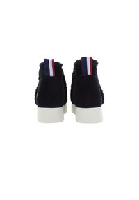 Schwarze Stiefeletten mit weißen Sohlen und rot-weiß-blauen Zugschlaufen, von hinten vor einem weißen Hintergrund betrachtet.